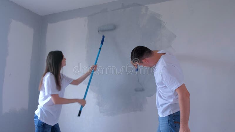 ζευγάρι νεαρός άνδρας και γυναίκα ζωγραφίζουν τον τοίχο με γκρι χρησιμοποιώντας ροδέλες μπογιάς. απόθεμα βίντεο