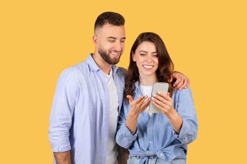 Happy man and woman looking at a mobile phone together with a yellow background. Happy man and woman looking at a mobile phone together with a yellow background