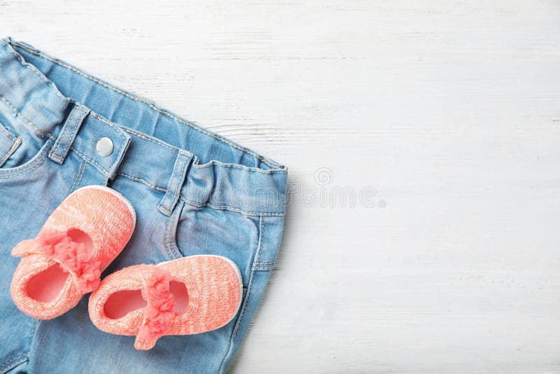 Ζευγάρι των χαριτωμένων σανδαλιών και των ενδυμάτων μωρών στον πίνακα στοκ εικόνα Ζευγάρι των χαριτωμένων σανδαλιών και των ενδυμάτων μωρών στον πίνακα στοκ εικόνα