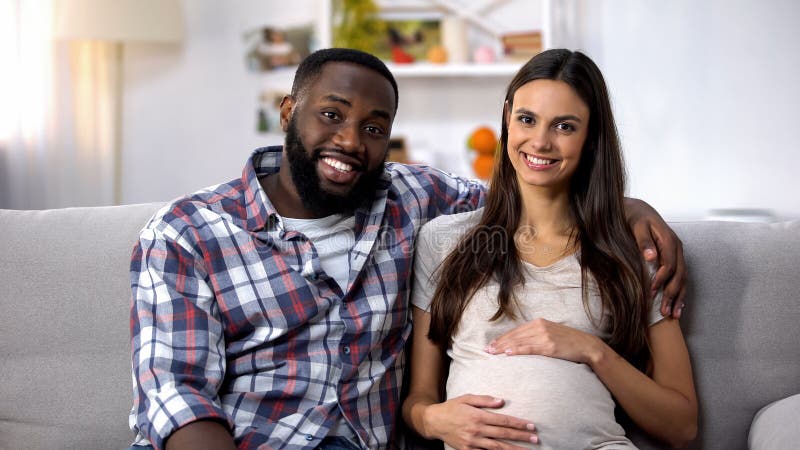 Ζεύγος Multiethnic που εξετάζει τη κάμερα, κοιλιά εκμετάλλευσης εγκύων γυναικών, ivf κλινική στοκ εικόνες Ζεύγος Multiethnic που εξετάζει τη κάμερα, κοιλιά εκμετάλλευσης εγκύων γυναικών, ivf κλινική στοκ εικόνες