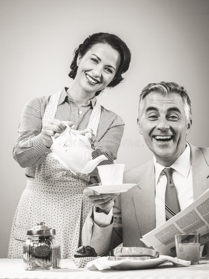 1950s beautiful women serving tea for breakfast to her smiling husband. 1950s beautiful women serving tea for breakfast to her smiling husband