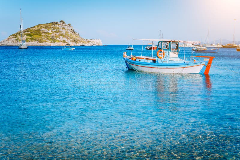 Ζωηρόχρωμο ελληνικό αλιευτικό σκάφος στο ήρεμο σαφές νερό στο πρωί αρχών του καλοκαιριού Άσπρος βράχος στο υπόβαθρο στοκ φωτογραφίες