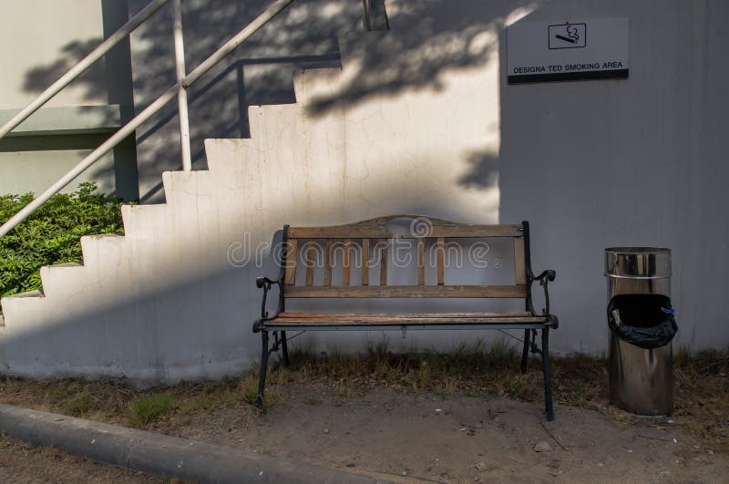 ζώνη καπνίσματος : ξύλινο παγκάκι με τασάκι για τους ανθρώπους που κάθονται να καπνίζουν τσιγάρο με ένα καθορισμένο σήμα χώρου καπ στοκ φωτογραφία