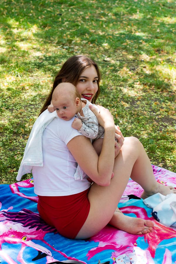 Η αγαπώντας μητέρα και το παιδί, νέο mom που φροντίζουν το χαριτωμένο μωρό της στα χέρια, προκλητικό mom κάθονται στο γενικό εξωτ στοκ εικόνα Η αγαπώντας μητέρα και το παιδί, νέο mom που φροντίζουν το χαριτωμένο μωρό της στα χέρια, προκλητικό mom κάθονται στο γενικό εξωτ στοκ εικόνα