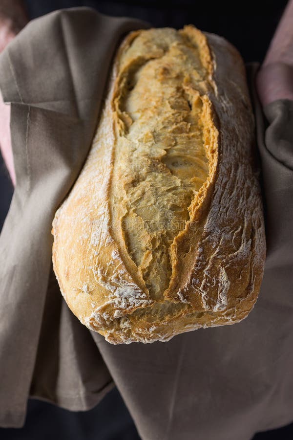 Η αρσενική εκμετάλλευση Baker παραδίδει μέσα την γκρίζα ψημένο πετσετών λινού πρόσφατα επεξεργασμένη χέρι αγροτική φραντζόλα ψωμι στοκ φωτογραφίες Η αρσενική εκμετάλλευση Baker παραδίδει μέσα την γκρίζα ψημένο πετσετών λινού πρόσφατα επεξεργασμένη χέρι αγροτική φραντζόλα ψωμι στοκ φωτογραφίες