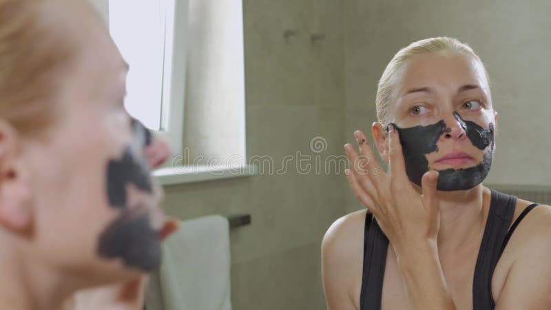 Η γυναίκα βάζει μια μάσκα λάσπης σε ένα πρόσωπο Φροντίδα προσώπου Διαδικασίες για ιαματικά λουτρά Σπα ημέρας Σχεδίαση μαύρης μάσκ