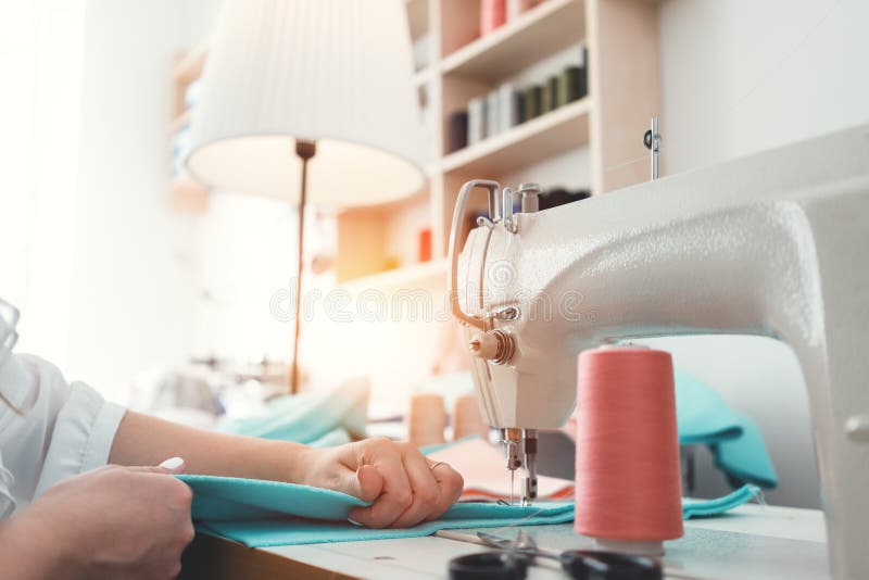 Η γυναίκα μοδιστρών ράβει τα ενδύματα στη ράβοντας μηχανή στο γραφείο σχεδίου Seamstress και χέρια κλείνουν επάνω στο εργαστήριο στοκ εικόνες Η γυναίκα μοδιστρών ράβει τα ενδύματα στη ράβοντας μηχανή στο γραφείο σχεδίου Seamstress και χέρια κλείνουν επάνω στο εργαστήριο στοκ εικόνες