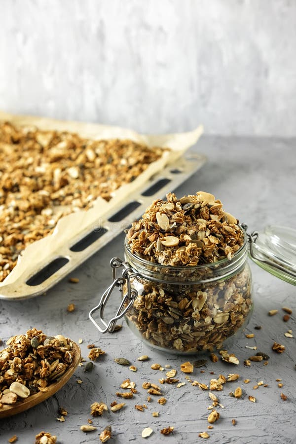 Η διαδικασία το σπιτικό granola Ένα βάζο γυαλιού, ένα ξύλινο κουτάλι και ένας δίσκος ψησίματος με ένα ξηρό πρόγευμα στοκ φωτογραφία με δικαίωμα ελεύθερης χρήσης Η διαδικασία το σπιτικό granola Ένα βάζο γυαλιού, ένα ξύλινο κουτάλι και ένας δίσκος ψησίματος με ένα ξηρό πρόγευμα στοκ φωτογραφία με δικαίωμα ελεύθερης χρήσης