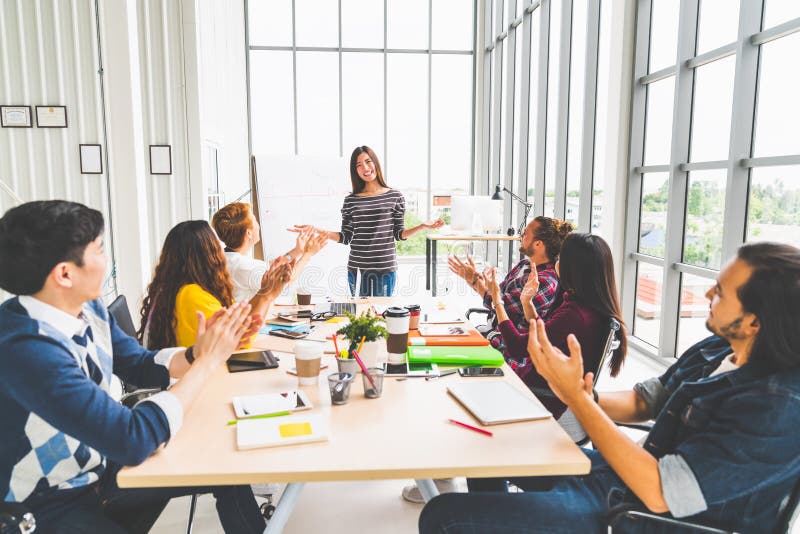 Multiethnic diverse group of creative team or business coworker clapping hands in project presentation meeting leading by Asian woman. Success teamwork, modern office work, or startup company concept. Multiethnic diverse group of creative team or business coworker clapping hands in project presentation meeting leading by Asian woman. Success teamwork, modern office work, or startup company concept