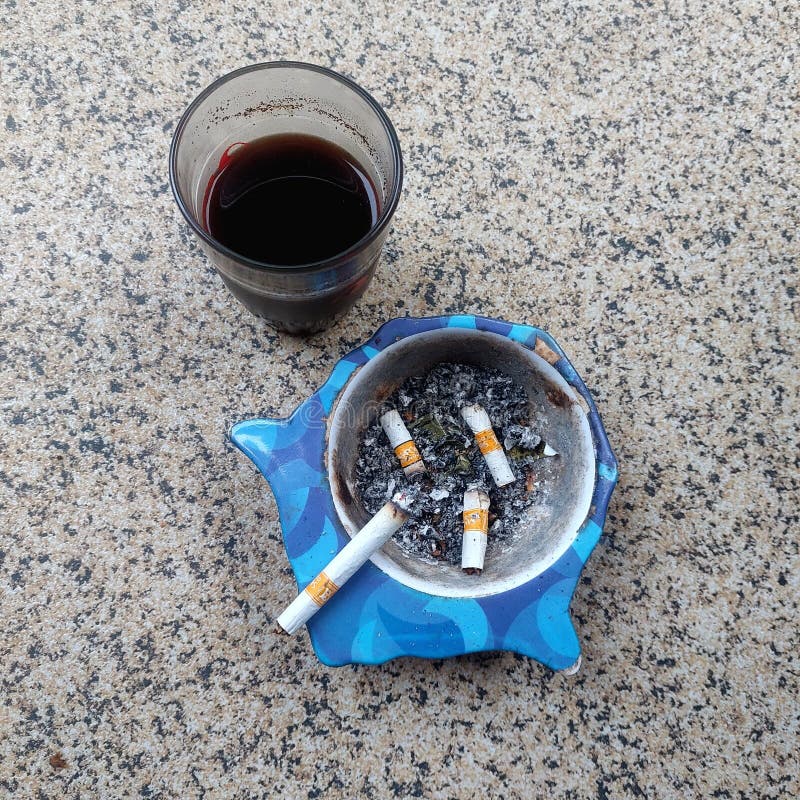 Η εικόνα δείχνει ένα ποτήρι γεμάτο με σκούρο μαύρο καφέ και ένα γαλάζιο τασάκι με τέσσερις γόβες. στοκ εικόνες