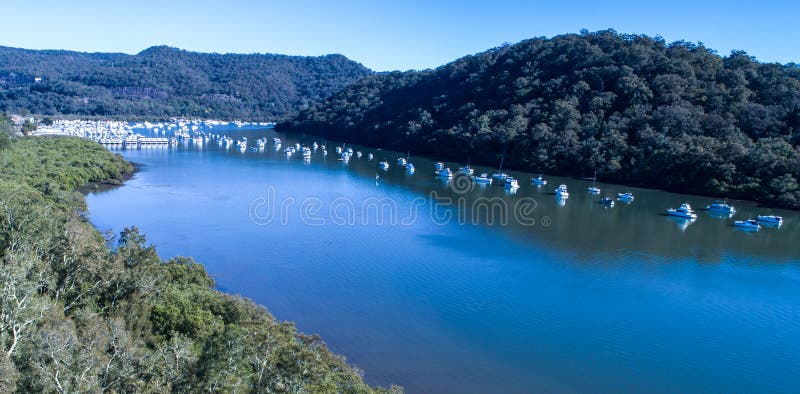 Η εναέρια άποψη των βαρκών έδεσε στον ποταμό Hawkesbury, Μπρούκλιν, Αυστραλία το μπλε νερό που περιβλήθηκε με από τα δέντρα γόμμα