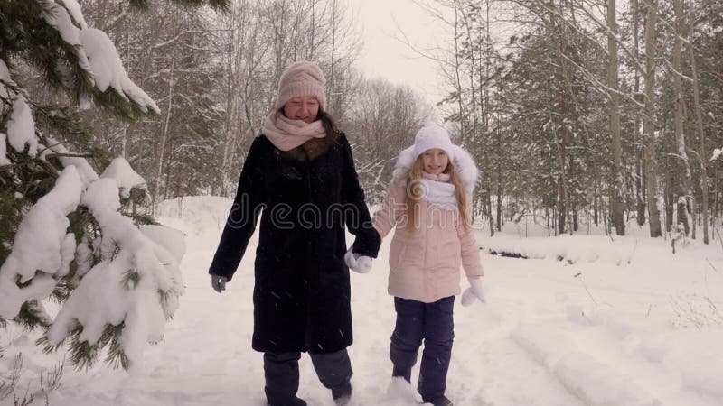 Η ευτυχείς μητέρα και η κόρη mom ενώνουν το χέρι και τον περίπατο μέσω χιονοπτώσεων ξύλων δέντρων πεύκων χειμερινών των δασικών π