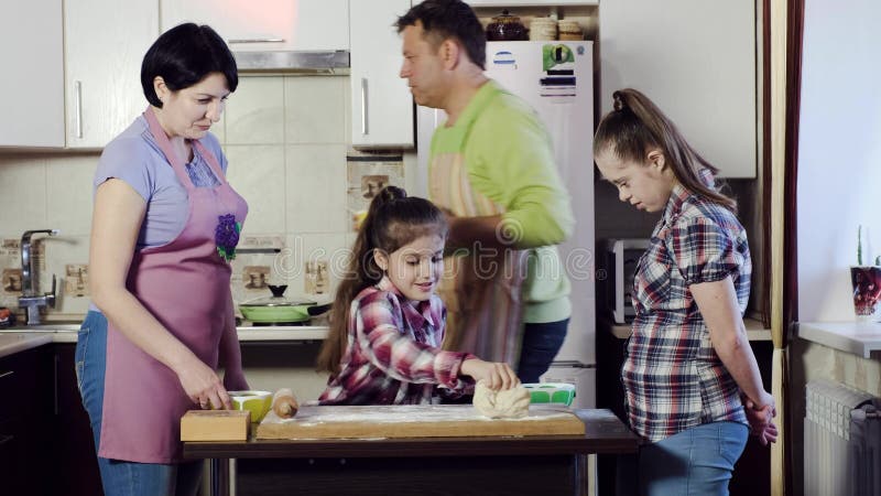 Η εύθυμη οικογένεια σε μια μικρή κουζίνα εξετάζει τη ζύμη