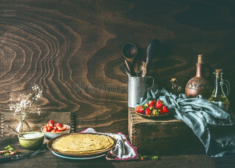Η ζωή χώρας ακόμα με σπιτικό crepes στο σκοτεινό αγροτικό ξύλινο πίνακα κουζινών με τις φράουλες και το γιαούρτι στοκ εικόνες