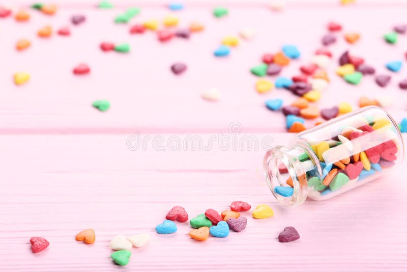 Colorful heart shaped sprinkles with glass bottle on pink wooden table