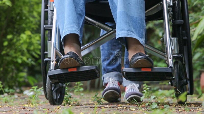 Ηλικιωμένη γυναίκα στην αναπηρική καρέκλα που περπατά με το caregiver απόθεμα βίντεο