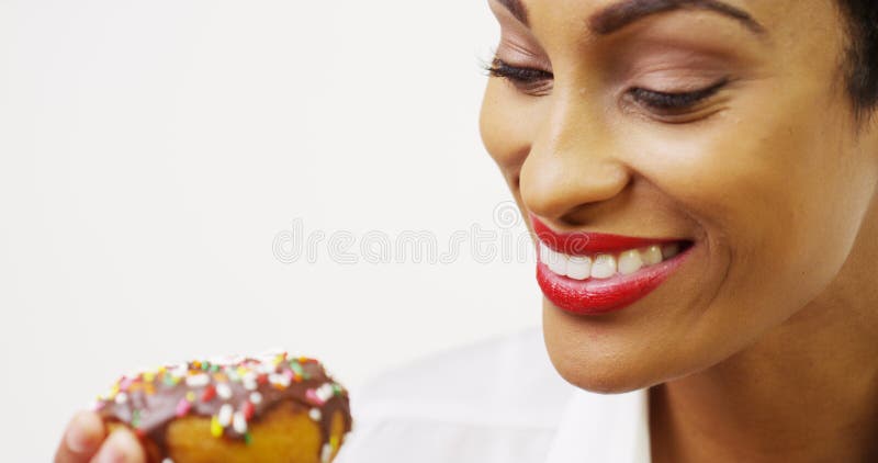 Η μαύρη γυναίκα που τρώει doughnut σοκολάτας με ψεκάζει και που χαμογελά στοκ φωτογραφία με δικαίωμα ελεύθερης χρήσης Η μαύρη γυναίκα που τρώει doughnut σοκολάτας με ψεκάζει και που χαμογελά στοκ φωτογραφία με δικαίωμα ελεύθερης χρήσης