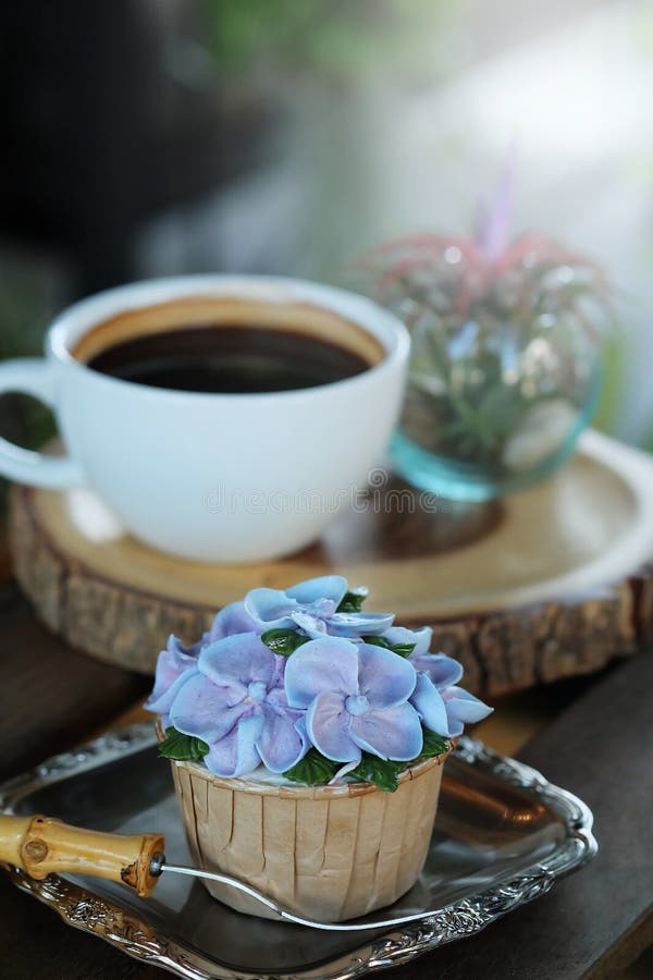 Η μπλε κρέμα σχεδίου cupcake όπως το μπλε λουλούδι Hydrangea εξυπηρέτησε με τον καυτό μαύρο καφέ στο ξύλινο επιτραπέζιο υπόβαθρο στοκ εικόνα με δικαίωμα ελεύθερης χρήσης Η μπλε κρέμα σχεδίου cupcake όπως το μπλε λουλούδι Hydrangea εξυπηρέτησε με τον καυτό μαύρο καφέ στο ξύλινο επιτραπέζιο υπόβαθρο στοκ εικόνα με δικαίωμα ελεύθερης χρήσης