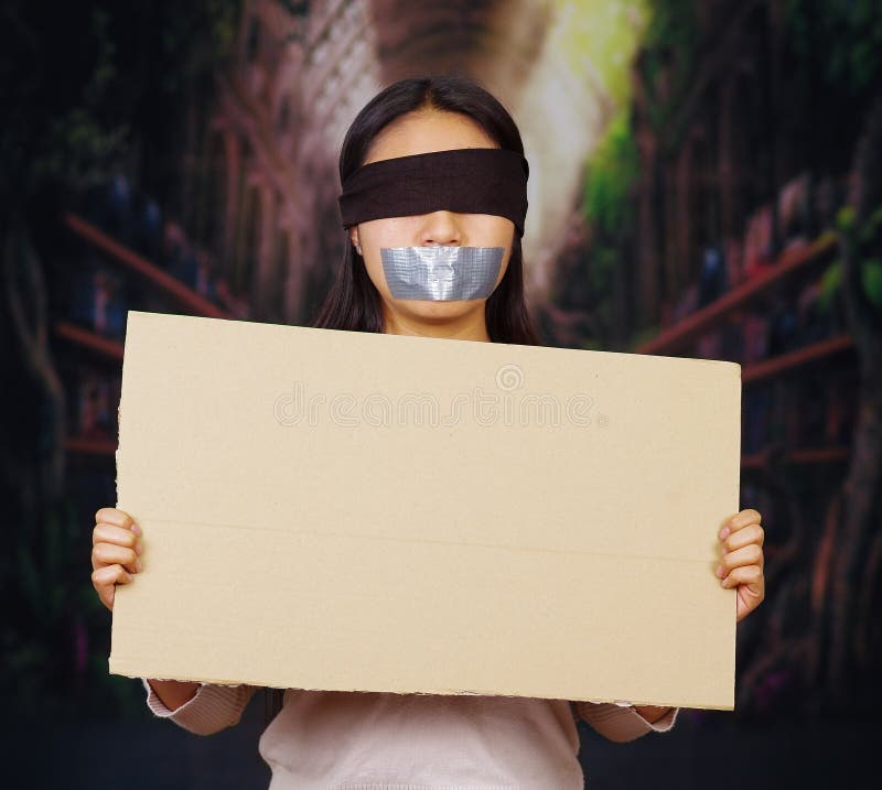 Η νέα γυναίκα brunette που φορά το άσπρο πουλόβερ, το μαύρο σχοινί και φίμωσε με την ταινία αγωγών, κρατώντας ψηλά το κενό σημάδι στοκ φωτογραφίες με δικαίωμα ελεύθερης χρήσης