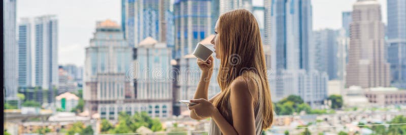 Η νέα γυναίκα πίνει τον καφέ το πρωί στο μπαλκόνι που αγνοεί το μεγάλο μακροχρόνιο σχήμα πόλεων και ΕΜΒΛΗΜΑΤΩΝ ουρανοξυστών στοκ φωτογραφίες με δικαίωμα ελεύθερης χρήσης