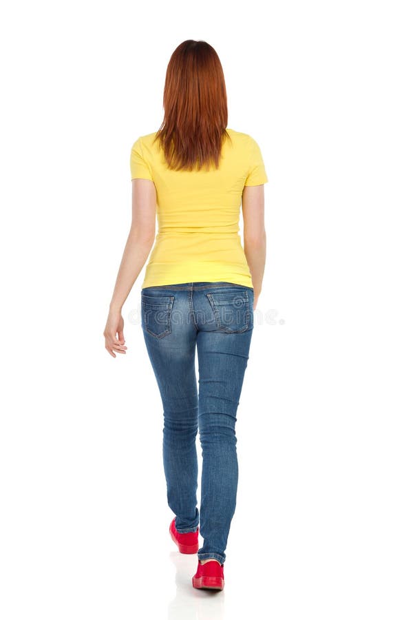 Η νέα γυναίκα στην κίτρινη μπλούζα, τα τζιν και τα κόκκινα πάνινα παπούτσια περπατά απομονωμένο οπισθοσκόπο λευκό