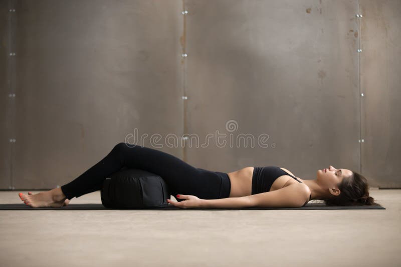 Η νέα ελκυστική γυναίκα που βρίσκεται σε Savasana θέτει τη χρησιμοποίηση του υποστυλώματος, stu στοκ εικόνα Η νέα ελκυστική γυναίκα που βρίσκεται σε Savasana θέτει τη χρησιμοποίηση του υποστυλώματος, stu στοκ εικόνα
