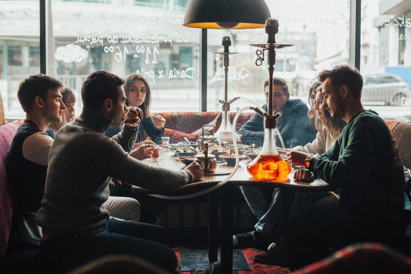 Η νέα επιχείρηση έχει τη διασκέδαση και τρώει στο φραγμό κάπνισμα ενός hookah, που επικοινωνεί σε ένα ασιατικό εστιατόριο στοκ εικόνες Η νέα επιχείρηση έχει τη διασκέδαση και τρώει στο φραγμό κάπνισμα ενός hookah, που επικοινωνεί σε ένα ασιατικό εστιατόριο στοκ εικόνες