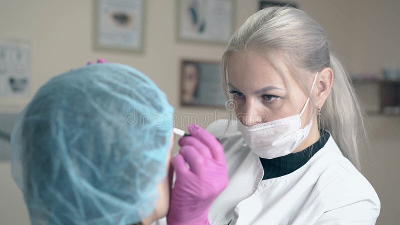Η ξανθή γυναίκα κάνει brow διαστίζοντας στο πρόσωπο πελατών στην κλινική
