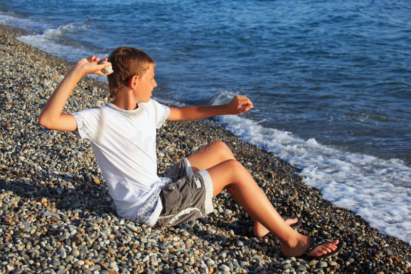 Sitting boy throws stone in sea, summer. Sitting boy throws stone in sea, summer