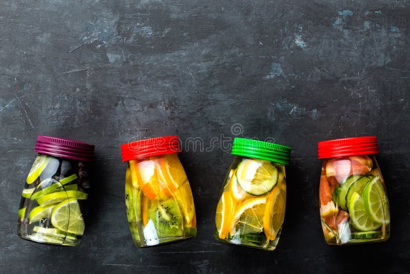 Variety of fruit infused detox water in jars for a healthy diet top view on a dark background with space for text. Variety of fruit infused detox water in jars for a healthy diet top view on a dark background with space for text