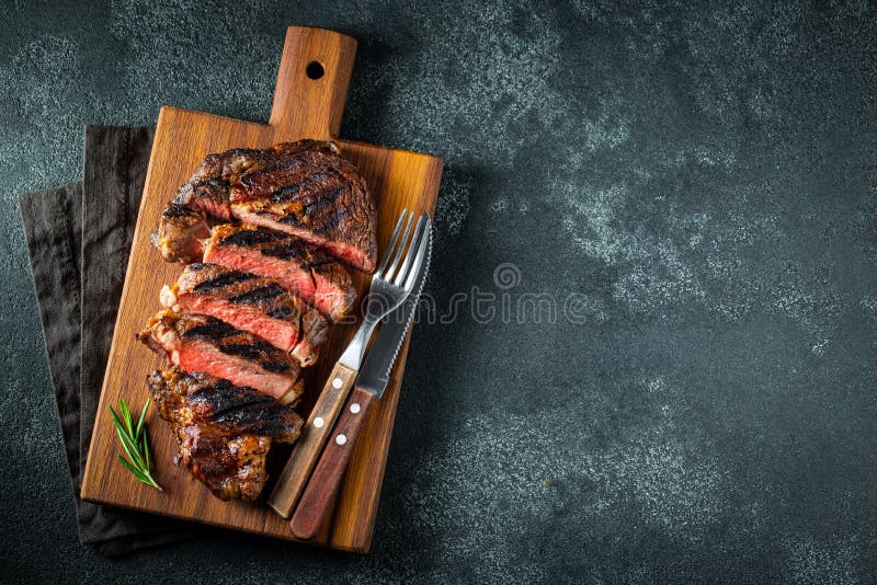 Η τεμαχισμένη μπριζόλα ribeye, ψημένος στη σχάρα με το πιπέρι, το σκόρδο, το αλάτι και το θυμάρι εξυπηρέτησε σε έναν ξύλινο τέμνο στοκ εικόνα με δικαίωμα ελεύθερης χρήσης Η τεμαχισμένη μπριζόλα ribeye, ψημένος στη σχάρα με το πιπέρι, το σκόρδο, το αλάτι και το θυμάρι εξυπηρέτησε σε έναν ξύλινο τέμνο στοκ εικόνα με δικαίωμα ελεύθερης χρήσης