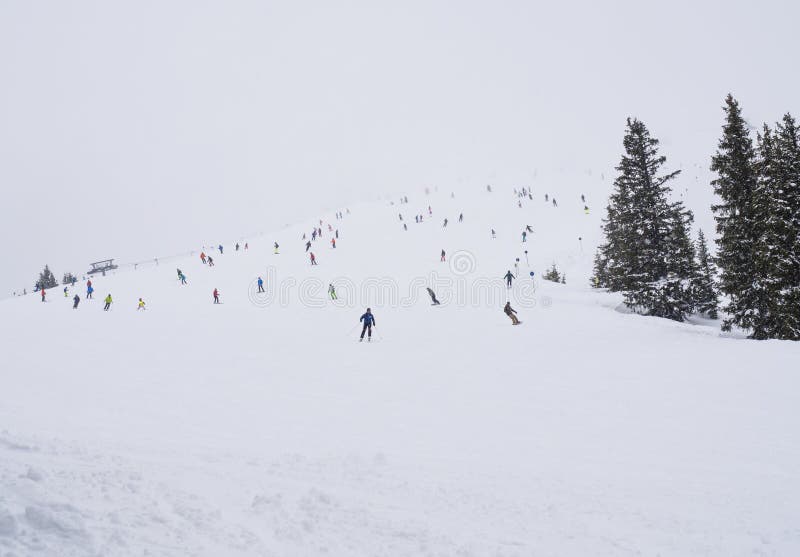 Η χιονισμένη κλίση σκι piste σε Zell AM βλέπει με το πλήθος των ζωηρόχρωμων σκιέρ την ομιχλώδη χειμερινή ημέρα, διάστημα αντιγράφ στοκ φωτογραφία με δικαίωμα ελεύθερης χρήσης Η χιονισμένη κλίση σκι piste σε Zell AM βλέπει με το πλήθος των ζωηρόχρωμων σκιέρ την ομιχλώδη χειμερινή ημέρα, διάστημα αντιγράφ στοκ φωτογραφία με δικαίωμα ελεύθερης χρήσης