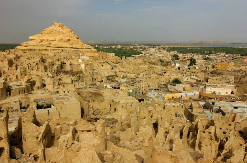 The Siwa Oasis is an oasis in Egypt, located between the Qattara Depression and the Egyptian Sand Sea in the Libyan Desert, nearly 50 km (30 mi) east of the Libyan border, and 560 km (348 mi) from Cairo. About 80 km (50 mi) in length and 20 km (12 mi) wide, [1] Siwa Oasis is one of Egypt's most isolated settlements, with 23, 000 people, mostly Berber speakers[1] who speak a distinct language of the Berber family known as Siwi. Its fame lies primarily in its ancient role as the home to an oracle of Amon, the ruins of which are a popular tourist attraction which gave the oasis its ancient name Ammonium. Historically, it is part of Ancient Libya. Its modern name Siwa, first attested in the 15th century (earlier Arab geographers termed it Santariyyah), is of uncertain origin. Agriculture is the main activity of modern Siwi, particularly the cultivation of dates and olives. Handicrafts like basketry are also of regional importance. The isolation of the oasis caused the development of a unique culture which was shown in its pottery, costume, styles of embroidery and, most notably, in the silver jewellery worn by women to weddings and important occasions. These pieces were decorated with symbols which related to Siwaâ€™s history and beliefs and attitudes. Tourism has in recent decades become a vital source of income. Much attention has been given to creating hotels that use local materials and play on local styles. The ancient fortress of Siwa, built on natural rock, made of salt, mud-brick and palm logs and known as the Shali Ghadi ("Shali" being the name of the town, and "Ghadi" meaning remote), although now mostly abandoned and 'melted', remains a prominent feature, towering five stories above the modern town. The Siwa Oasis is an oasis in Egypt, located between the Qattara Depression and the Egyptian Sand Sea in the Libyan Desert, nearly 50 km (30 mi) east of the Libyan border, and 560 km (348 mi) from Cairo. About 80 km (50 mi) in length and 20 km (12 mi) wide, [1] Siwa Oasis is one of Egypt's most isolated settlements, with 23, 000 people, mostly Berber speakers[1] who speak a distinct language of the Berber family known as Siwi. Its fame lies primarily in its ancient role as the home to an oracle of Amon, the ruins of which are a popular tourist attraction which gave the oasis its ancient name Ammonium. Historically, it is part of Ancient Libya. Its modern name Siwa, first attested in the 15th century (earlier Arab geographers termed it Santariyyah), is of uncertain origin. Agriculture is the main activity of modern Siwi, particularly the cultivation of dates and olives. Handicrafts like basketry are also of regional importance. The isolation of the oasis caused the development of a unique culture which was shown in its pottery, costume, styles of embroidery and, most notably, in the silver jewellery worn by women to weddings and important occasions. These pieces were decorated with symbols which related to Siwaâ€™s history and beliefs and attitudes. Tourism has in recent decades become a vital source of income. Much attention has been given to creating hotels that use local materials and play on local styles. The ancient fortress of Siwa, built on natural rock, made of salt, mud-brick and palm logs and known as the Shali Ghadi ("Shali" being the name of the town, and "Ghadi" meaning remote), although now mostly abandoned and 'melted', remains a prominent feature, towering five stories above the modern town.