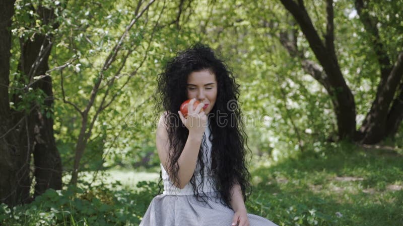 Η όμορφη γυναίκα τρώει τη φρέσκια συνεδρίαση μήλων στο θερινό κήπο