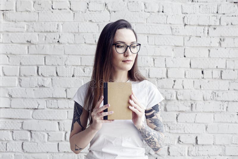 Η όμορφη διαστισμένη hipster γυναίκα θέτει στην άσπρη μπλούζα με το βιβλίο ι στοκ εικόνες Η όμορφη διαστισμένη hipster γυναίκα θέτει στην άσπρη μπλούζα με το βιβλίο ι στοκ εικόνες