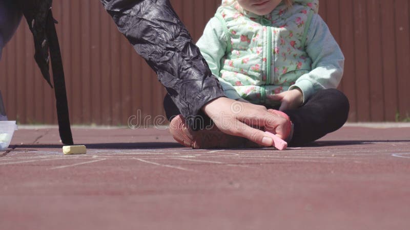Η όμορφη καυκάσια μητέρα επισύρει την προσοχή με τα κραγιόνια με την λίγη κόρη 3 χρονών στην παιδική χαρά, παιχνίδι