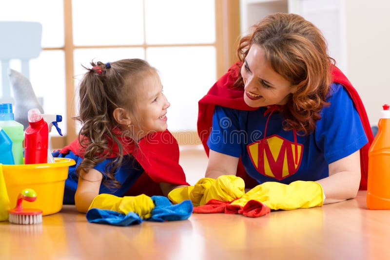 Η όμορφη μητέρα και η χαριτωμένη κόρη παιδιών έντυσαν όπως τα superheroes Γυναίκα και παιδί έτοιμες στον καθαρισμό του σπιτιού