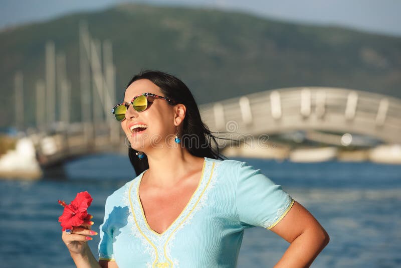 Η όμορφη στάση γυναικών κοντά στη γέφυρα στην πόλη της Λευκάδας, το χαμόγελο και το κράτημα κόκκινων hibiscus ανθίζουν, στοκ εικόνες με δικαίωμα ελεύθερης χρήσης Η όμορφη στάση γυναικών κοντά στη γέφυρα στην πόλη της Λευκάδας, το χαμόγελο και το κράτημα κόκκινων hibiscus ανθίζουν, στοκ εικόνες με δικαίωμα ελεύθερης χρήσης
