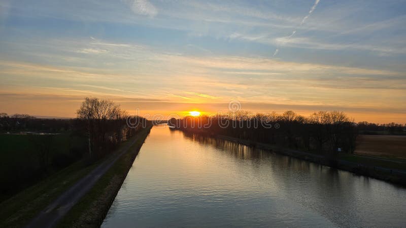 The afterglow paints the sky as the sun sets over the river, casting a beautiful reflection on the water surrounded by. The afterglow paints the sky as the sun sets over the river, casting a beautiful reflection on the water surrounded by