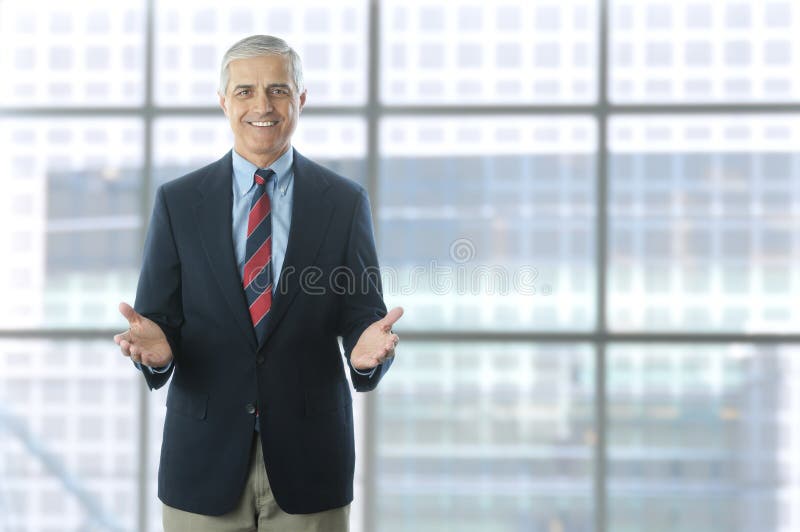 Smiling middle aged businessman standing in the lobby of a modern office building. Man is wearing a blue blazer and khaki pants and gesturing with both hands. Horizontal Format. Smiling middle aged businessman standing in the lobby of a modern office building. Man is wearing a blue blazer and khaki pants and gesturing with both hands. Horizontal Format.