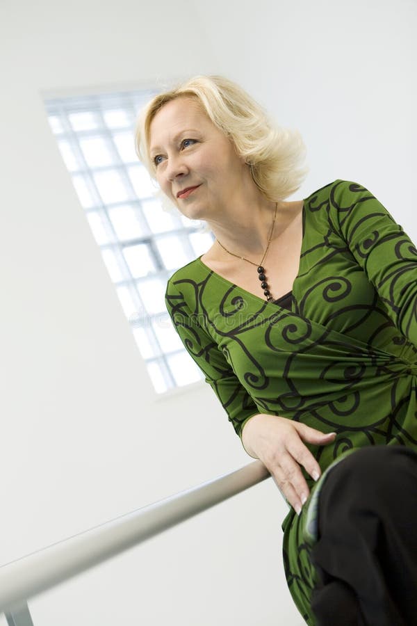 A portrait of an attractive blond middle aged woman wearing a green print dress in a bright white room. A portrait of an attractive blond middle aged woman wearing a green print dress in a bright white room.