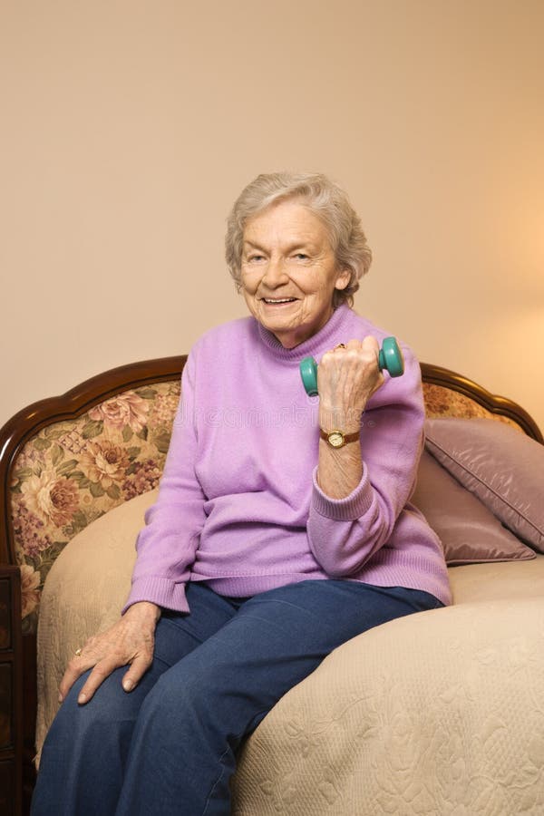 Elderly Caucasian woman in her bedroom at retirement community center lifting weights to strengthen arms. Elderly Caucasian woman in her bedroom at retirement community center lifting weights to strengthen arms.