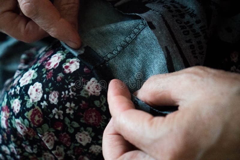 Ηλικιωμένη γυναίκα με τα χέρια να ράψουν στο ύφασμα, τη βελόνα Ράψτε παντελόνια με το χέρι της γριάς, γκαζώστε στη δουλειά με ύφα στοκ φωτογραφία Ηλικιωμένη γυναίκα με τα χέρια να ράψουν στο ύφασμα, τη βελόνα Ράψτε παντελόνια με το χέρι της γριάς, γκαζώστε στη δουλειά με ύφα στοκ φωτογραφία