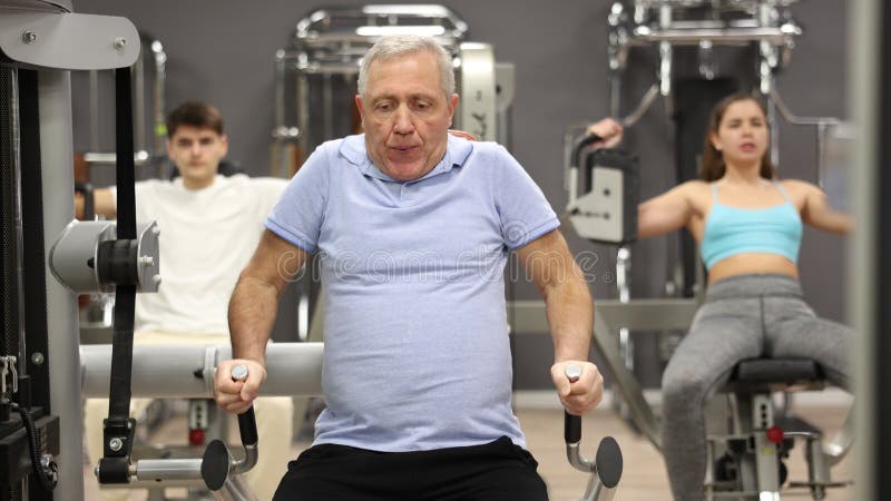 ηλικιωμένος ενεργός άνδρας που ασκεί άσκηση σε προσομοιωτή σε σύγχρονο γυμναστήριο