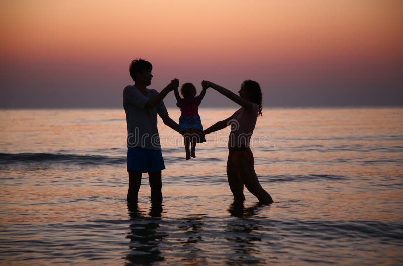 Father with mother hold child in sea on sunset. Father with mother hold child in sea on sunset