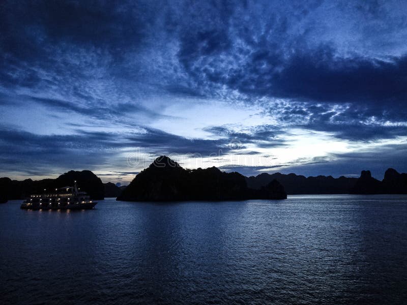 Ηλιοβασίλεμα στον κόλπο Halong Με ένα φωτισμένο σκάφος στο υπόβαθρο και τον μπλε δραματικού ουρανό τόνων και στοκ φωτογραφίες με δικαίωμα ελεύθερης χρήσης Ηλιοβασίλεμα στον κόλπο Halong Με ένα φωτισμένο σκάφος στο υπόβαθρο και τον μπλε δραματικού ουρανό τόνων και στοκ φωτογραφίες με δικαίωμα ελεύθερης χρήσης