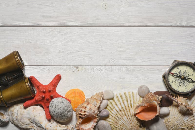 Vintage compass, binoculars, seashells and pebble stones on the white wooden desk table close up background with copy space. Vintage compass, binoculars, seashells and pebble stones on the white wooden desk table close up background with copy space