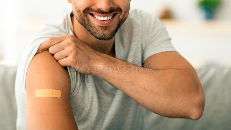 Θετικός νεαρός εμβολιασμένος άνδρας επιδεικνύει τον ώμο του με ιατρικό γύψο μετά την ένεση του εμβολίου χαμογελώντας στην κάμερα στοκ εικόνες με δικαίωμα ελεύθερης χρήσης