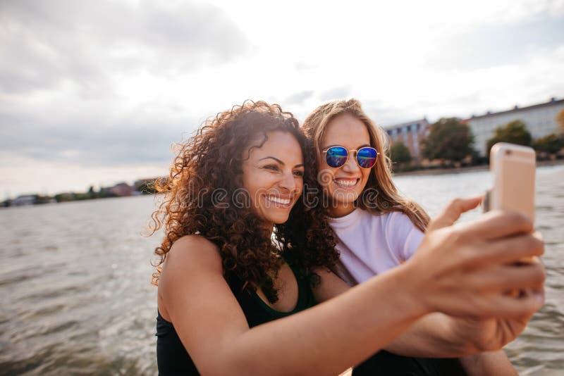Θηλυκοί φίλοι που παίρνουν selfie με το κινητό τηλέφωνο από τη λίμνη στοκ εικόνες