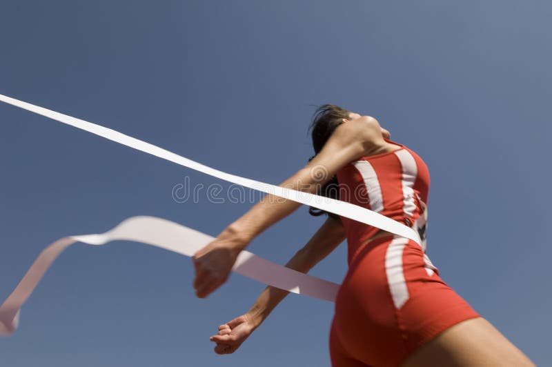 Θηλυκός αθλητής που διασχίζει τη γραμμή τερματισμού ενάντια στο μπλε ουρανό στοκ εικόνες